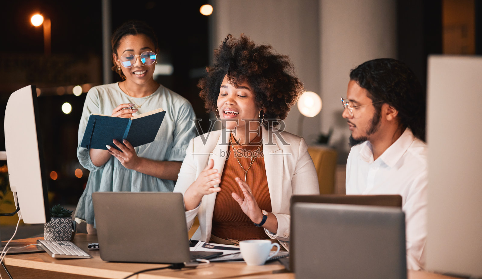 笔记本电脑，晚上和团队在办公室讨论一个有截止日期的创意网站项目。对话，规划和专业设计师在工作场所的电脑上加班。照片摄影图片