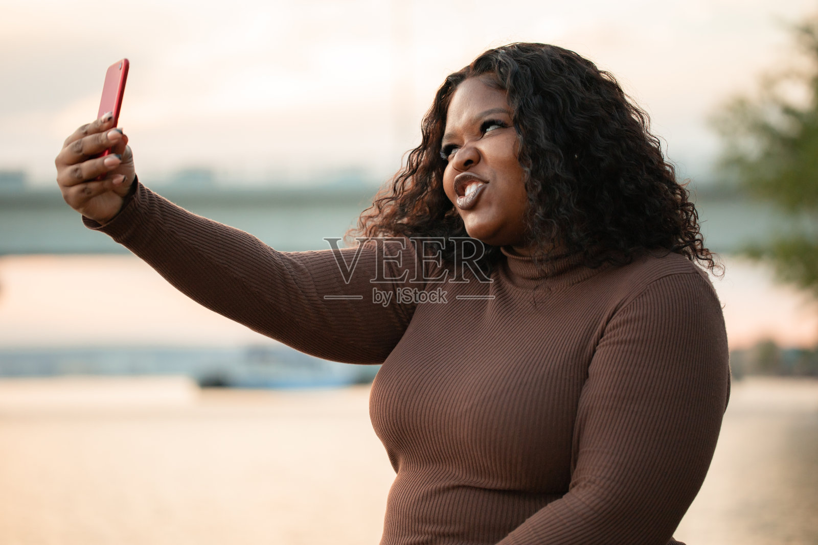 卷发自信的现代多元文化的黑皮肤女人穿着裙子在手网上自拍，摆姿势，做鬼脸。身体正照片摄影图片