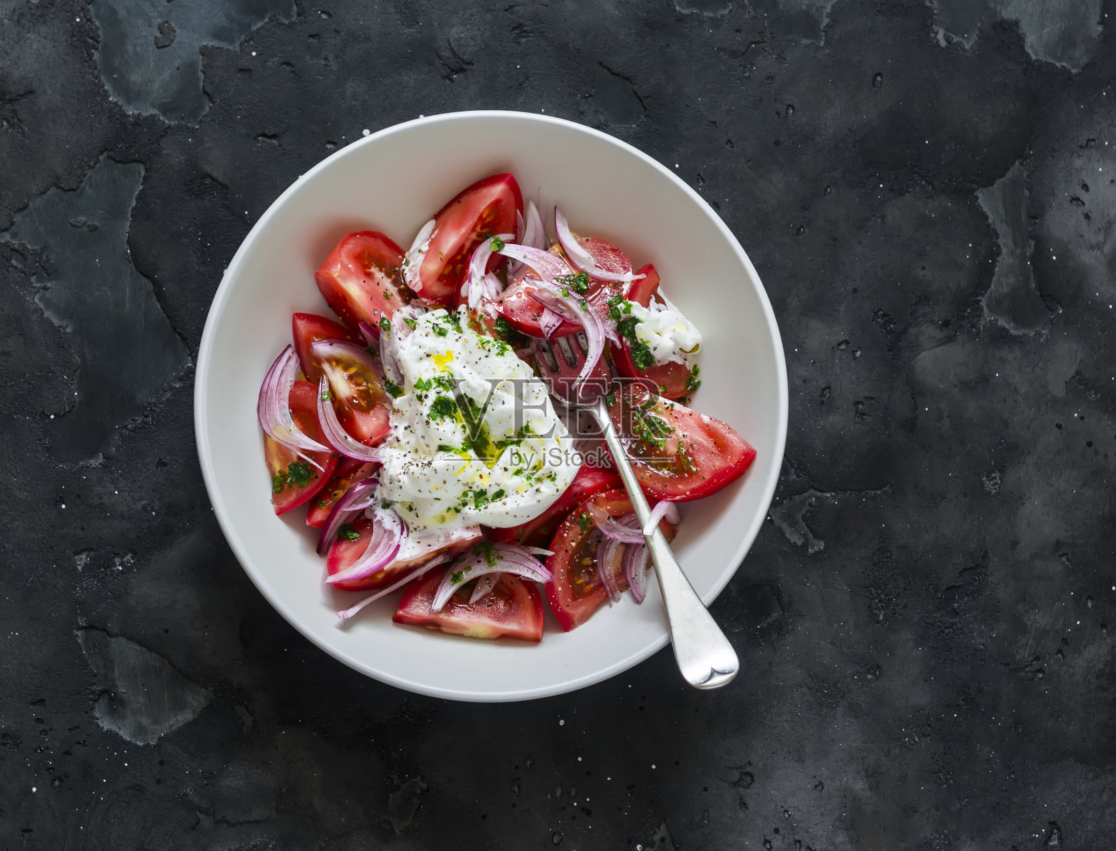 沙拉中有新鲜的西红柿、布拉塔奶酪、红洋葱和香蒜沙司，背景为深色，俯视图照片摄影图片
