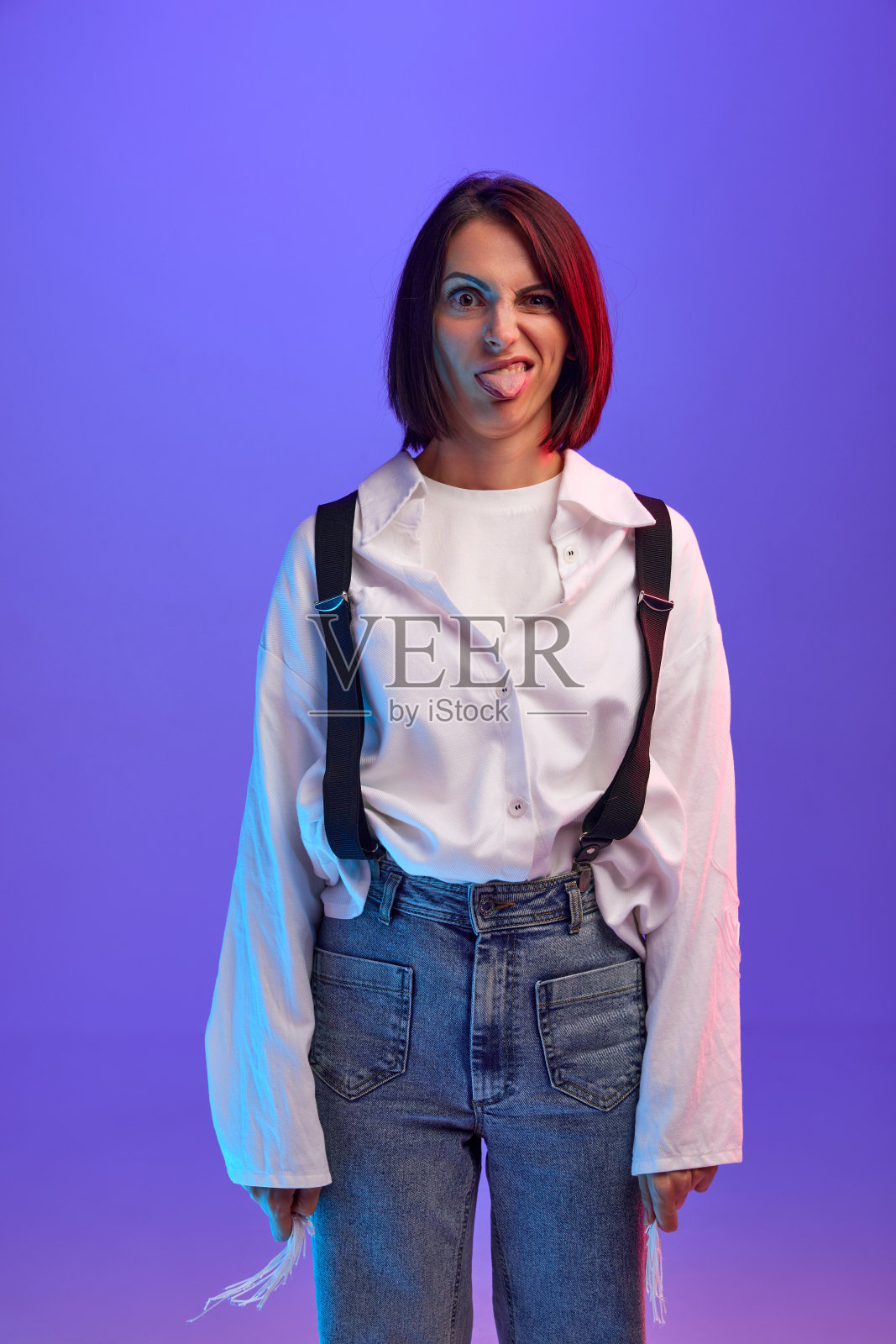 有趣的表情包脸。30多岁的时尚感性女性的肖像，在霓虹灯的紫色工作室背景下摆着滑稽的脸照片摄影图片