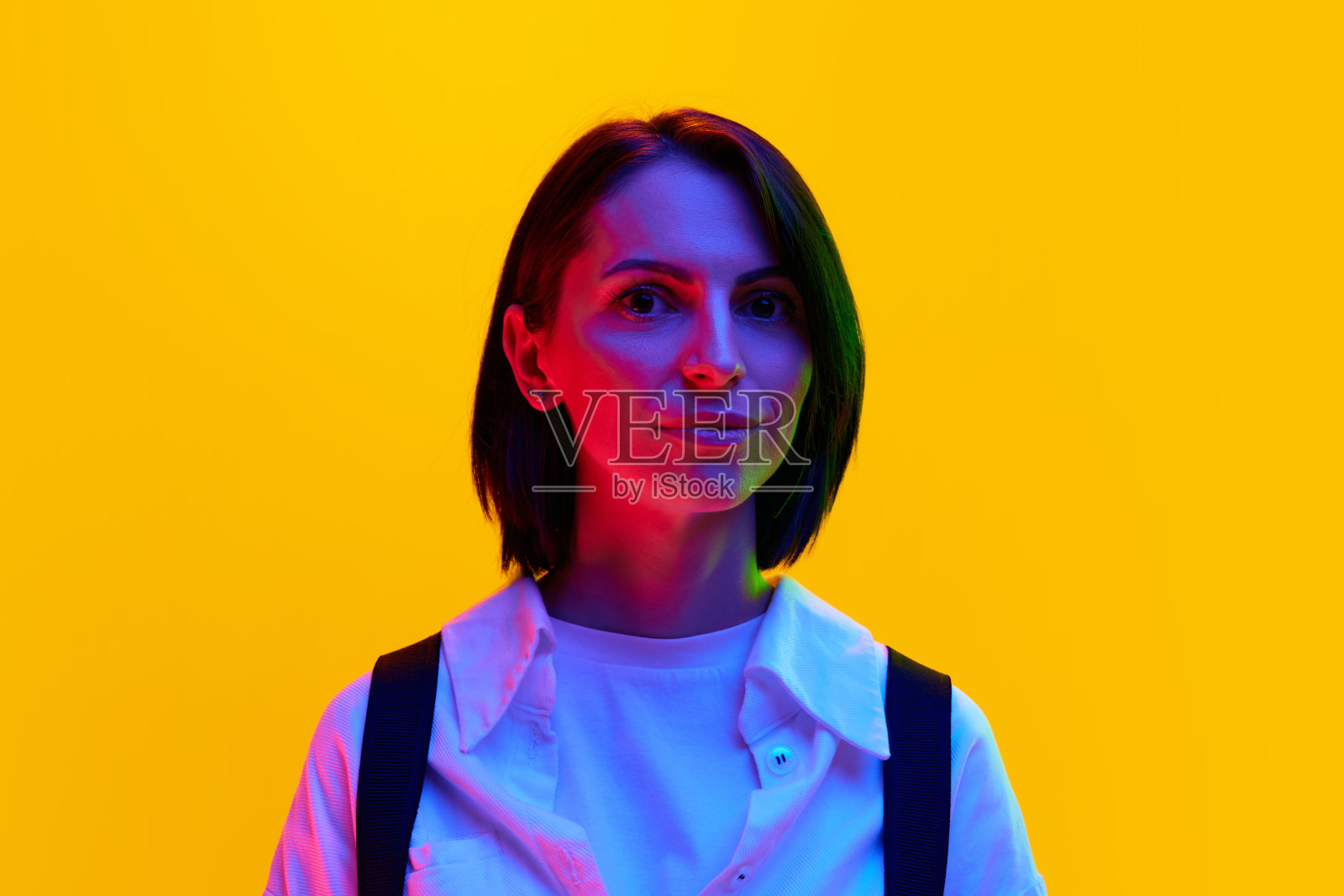 一个30多岁的女人，穿着白衬衫，在霓虹灯的橙色工作室背景下带着微笑看着镜头照片摄影图片