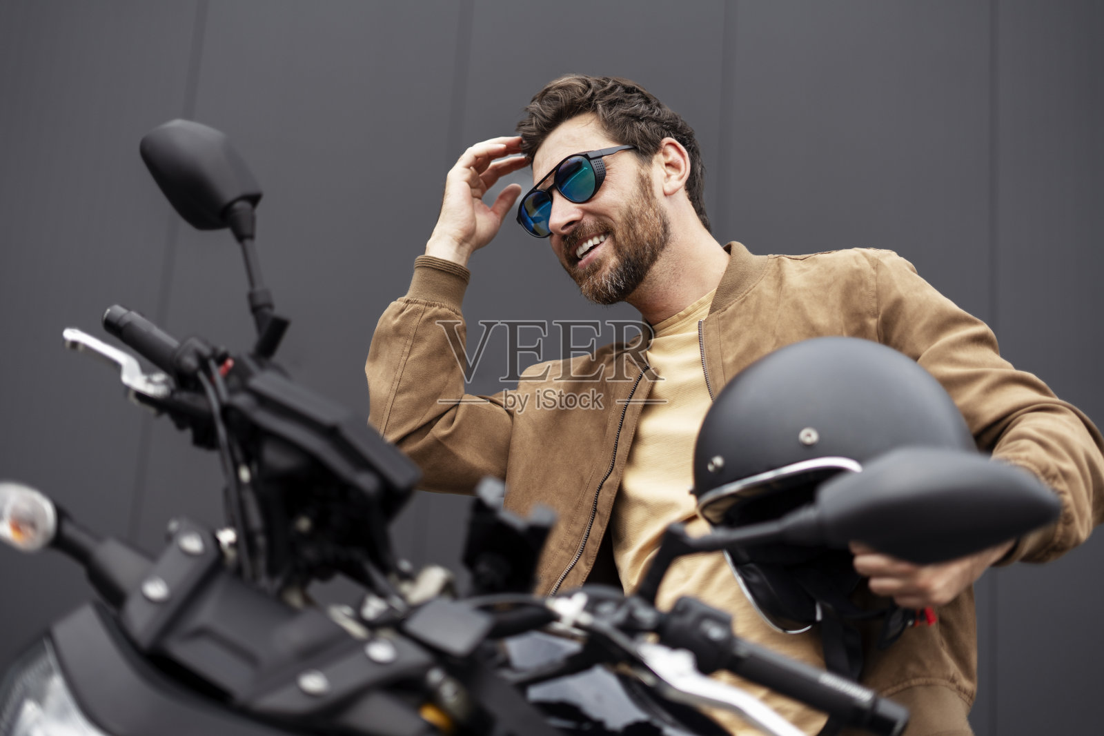 时尚微笑自信的男人，骑摩托车的人拿着头盔坐在运动摩托车上照片摄影图片