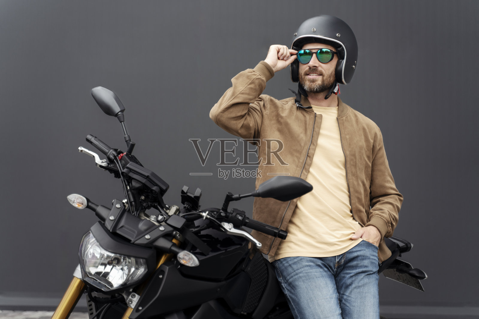 凶残的大胡子男子，戴着头盔的摩托车手站在街上的运动摩托车旁边照片摄影图片