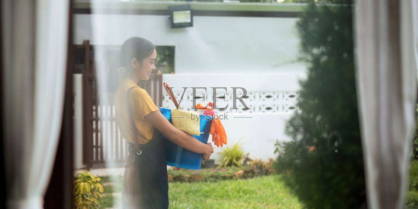 一名清洁女工站在一栋建筑里，手里拿着一个装满化学药品和清洁设备的蓝色水桶。管理的概念照片摄影图片