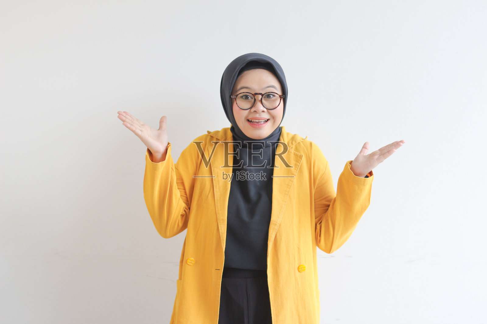 年轻漂亮的亚洲穆斯林妇女，戴着眼镜，穿着黄色运动夹克，脸上带着震惊的表情照片摄影图片