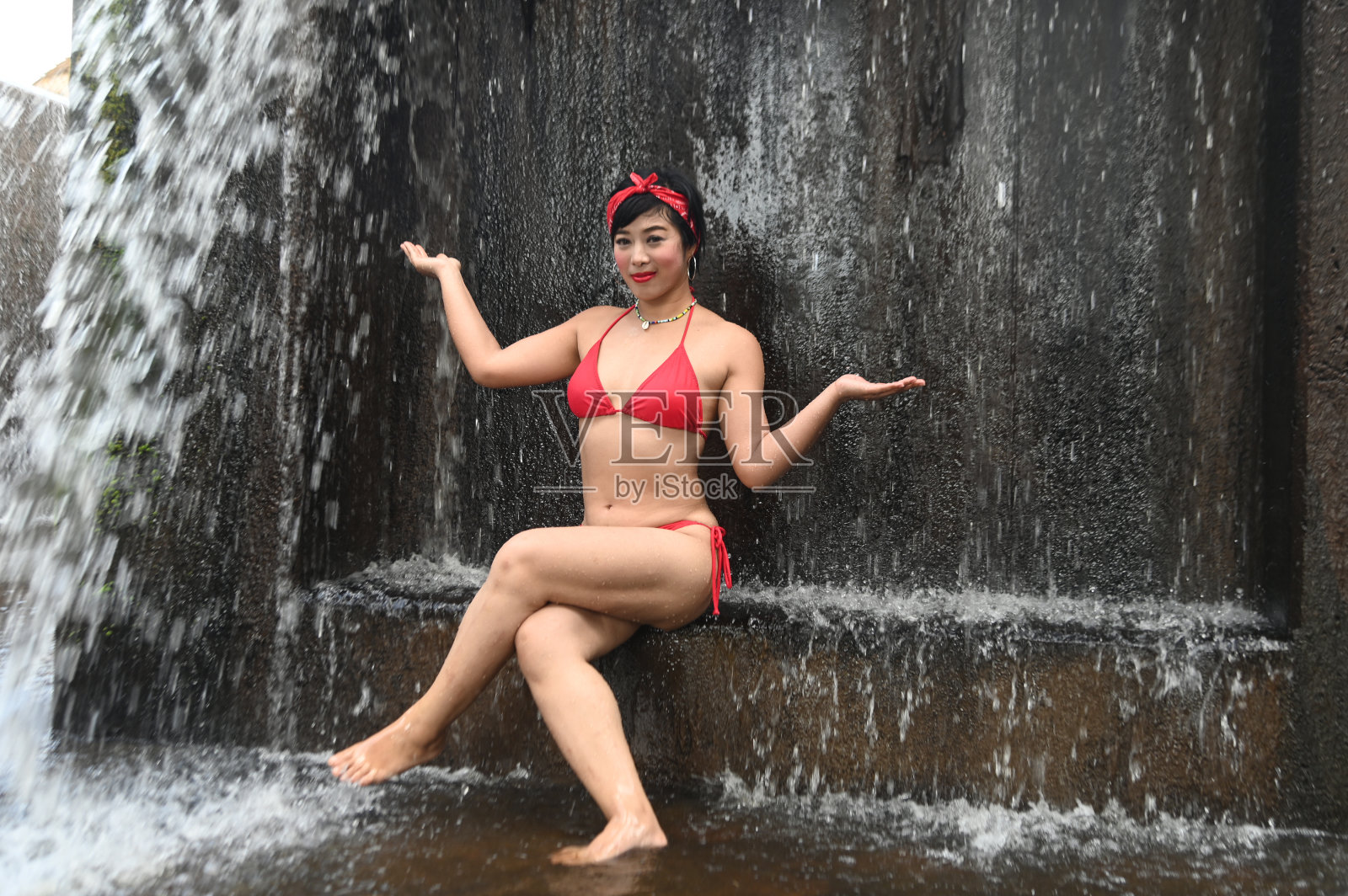 一个漂亮的亚洲女性穿着泳衣坐着，放松地展示着她的乐趣。在泰国的一个溢洪道。照片摄影图片