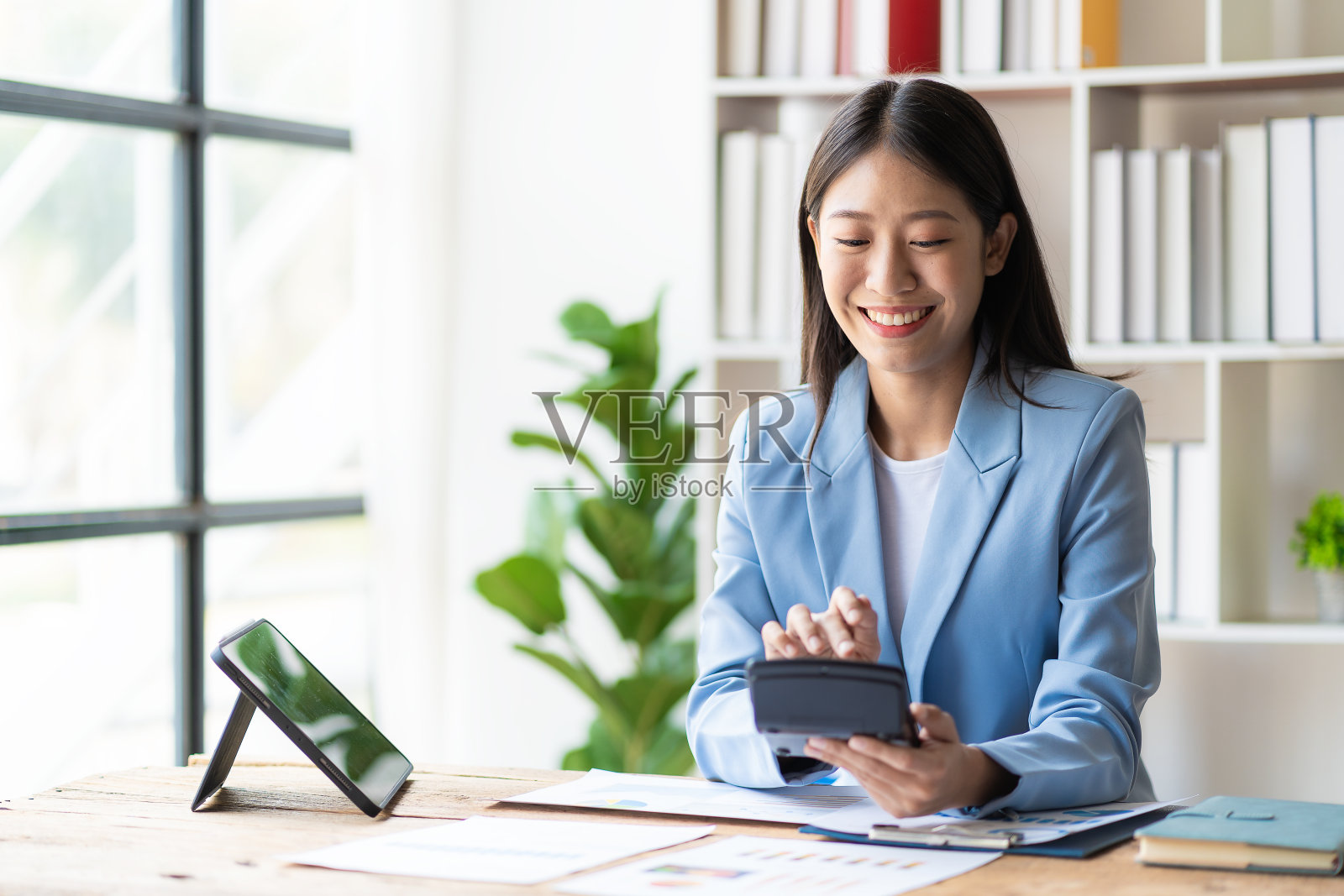 快乐的年轻亚洲女商人，用笔记本电脑和智能手机处理财务文件照片摄影图片
