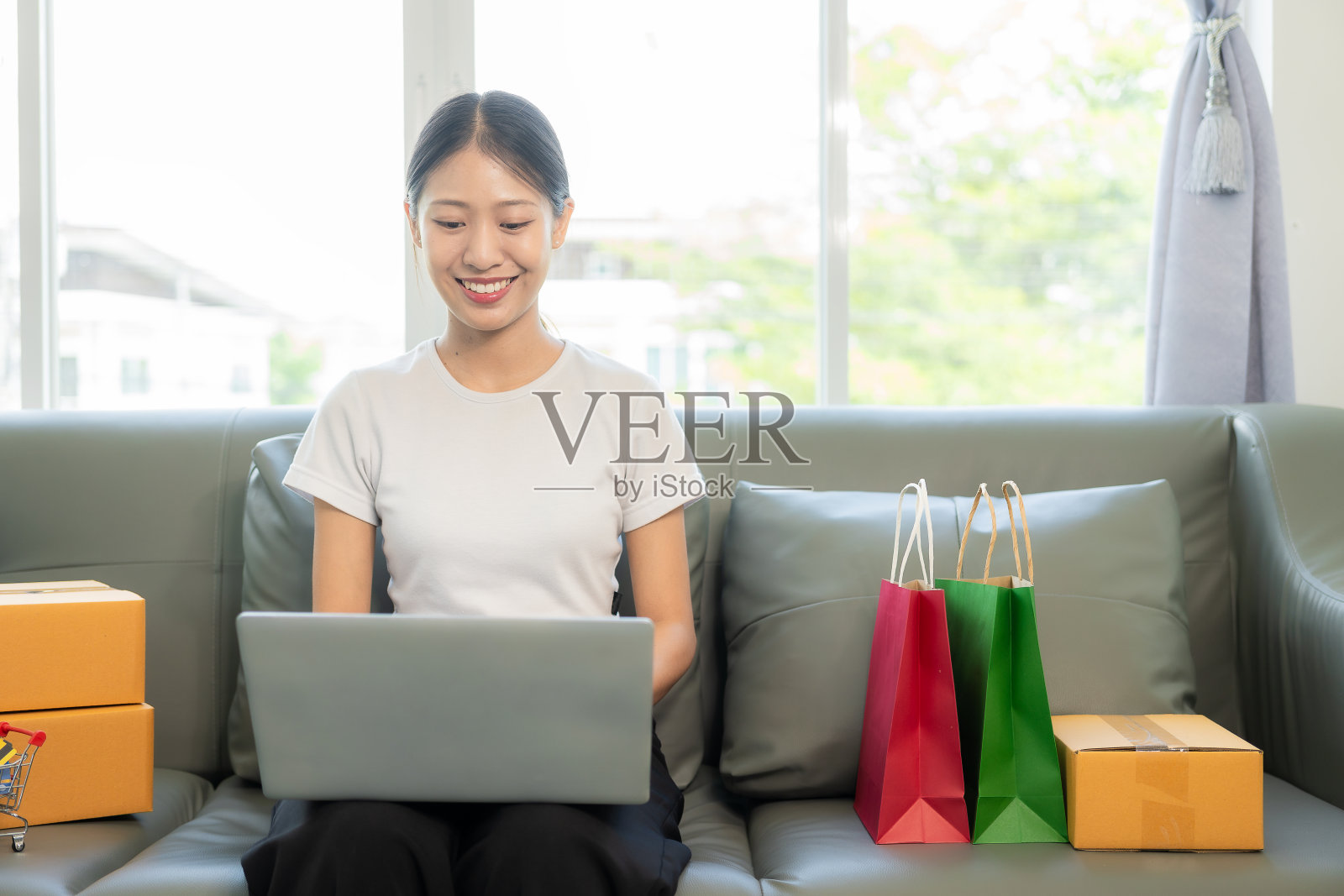 亚洲女性拿着信用卡、智能手机和笔记本电脑坐在家里的沙发上进行网上银行交易照片摄影图片