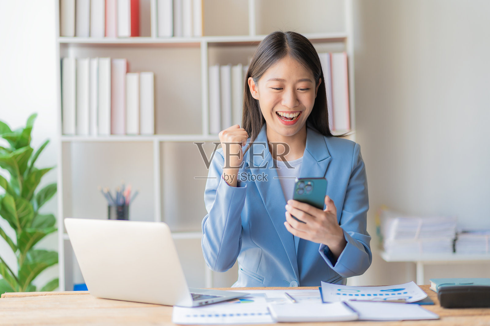 快乐的年轻亚洲女商人，用笔记本电脑和智能手机处理财务文件照片摄影图片