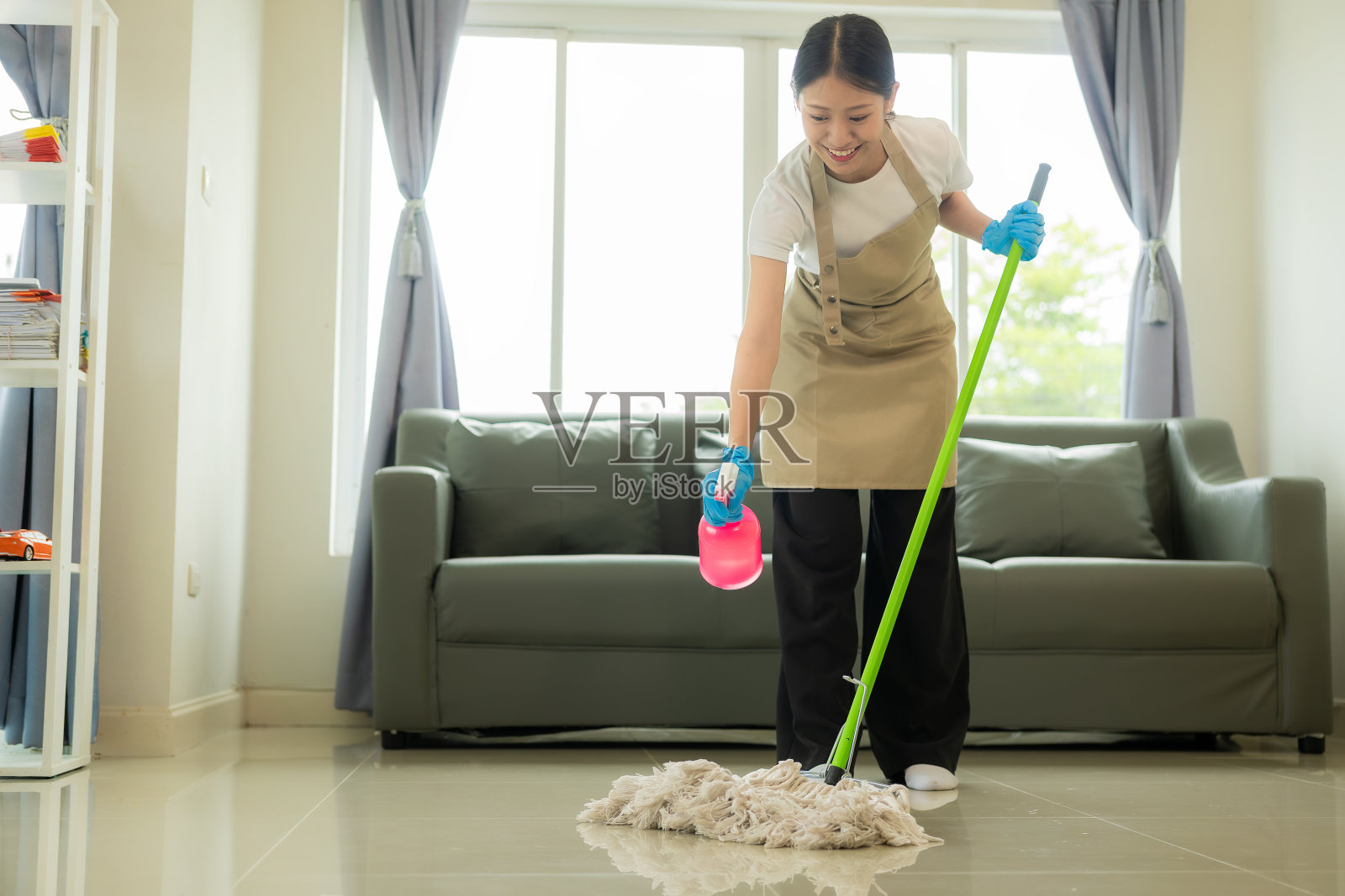 年轻的亚洲妇女享受春季大扫除的房子或公寓，家务和家政概念-快乐的亚洲妇女或家庭主妇用拖把打扫房子。照片摄影图片