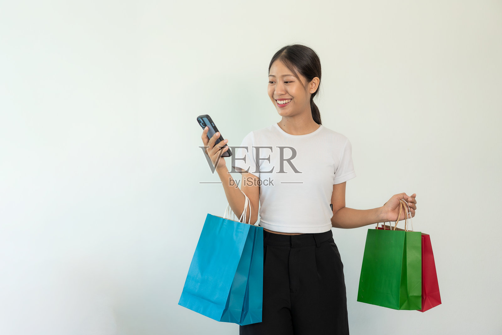 手持信用卡的亚洲女性智能手机，白色屏幕和购物袋，白色背景，网上银行交易概念在网上购物照片摄影图片