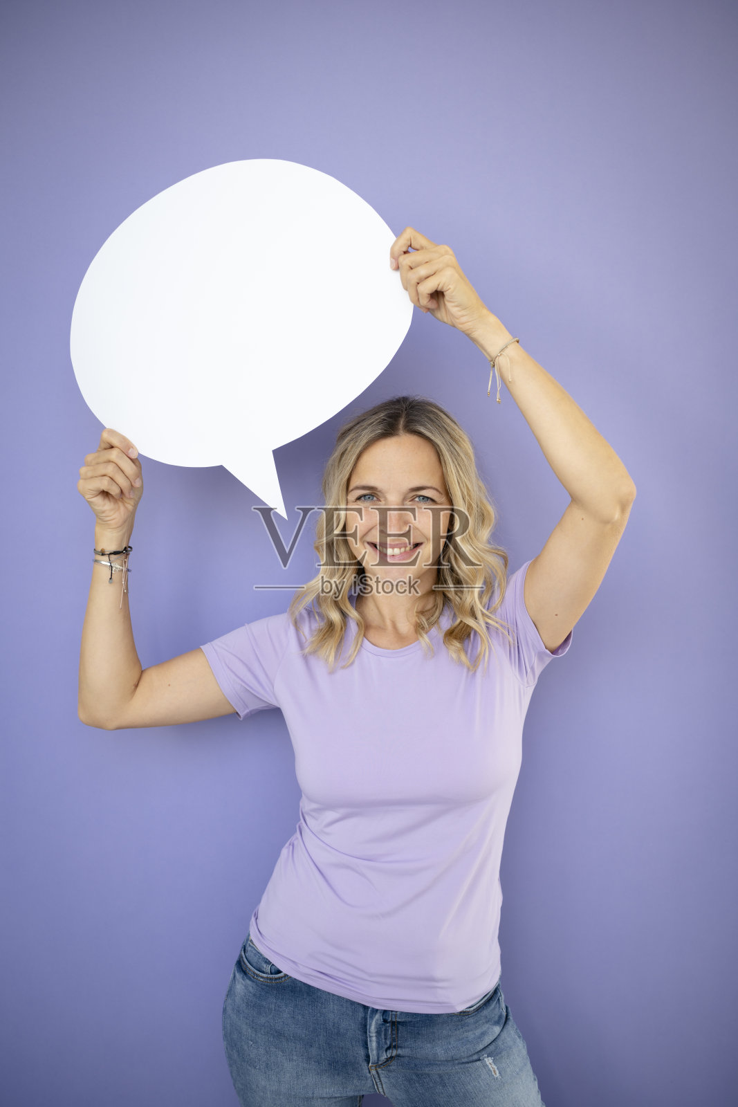 年轻漂亮的卷发女子，捧着白色的话泡，站在紫罗兰前面，紫色的背景照片摄影图片