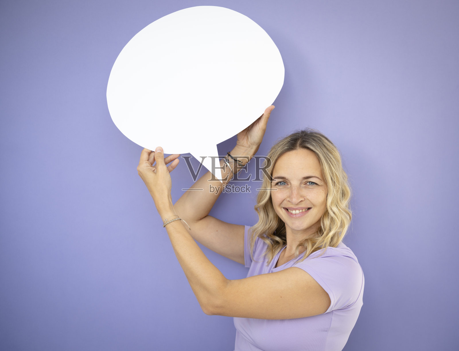 年轻漂亮的卷发女子，捧着白色的话泡，站在紫罗兰前面，紫色的背景照片摄影图片