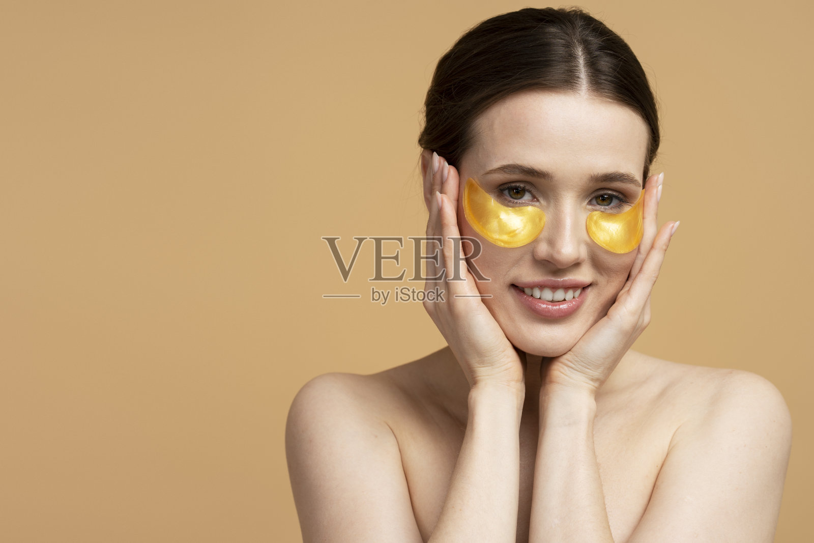 微笑的白人妇女用金色的眼罩，在米色的背景上孤立照片摄影图片