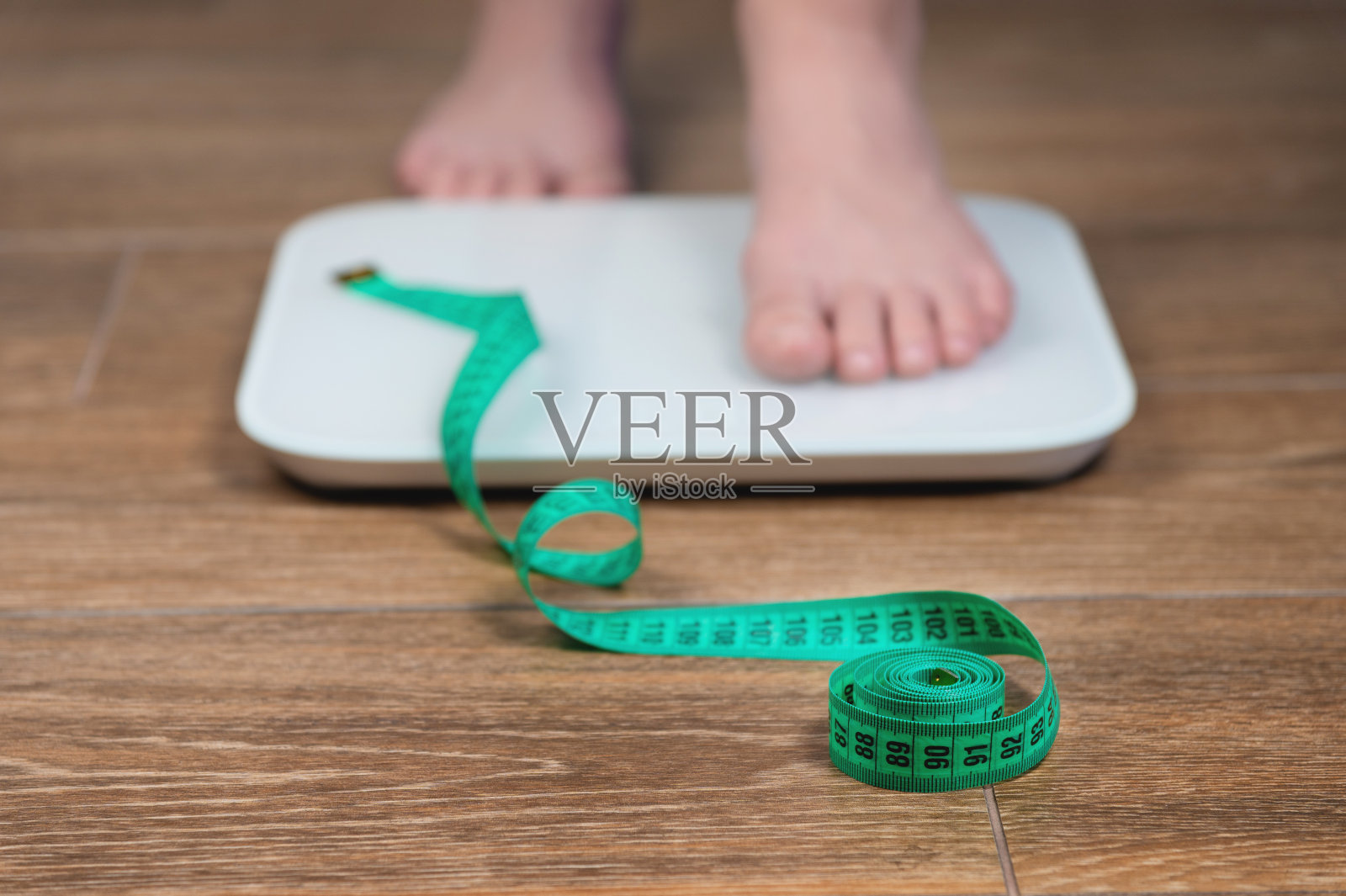 拿着卷尺站在秤上的女人，特写。饮食，健康的生活方式，减肥，苗条的理念。站在磅秤上的人的腿的特写照片摄影图片
