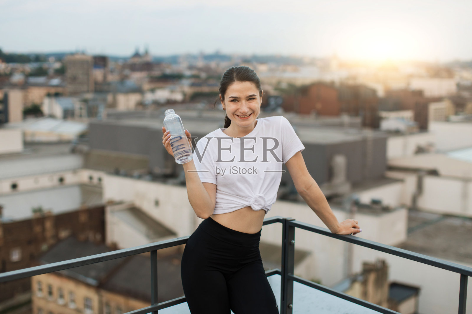 瑜伽行者拿着水瓶在楼顶看日落照片摄影图片