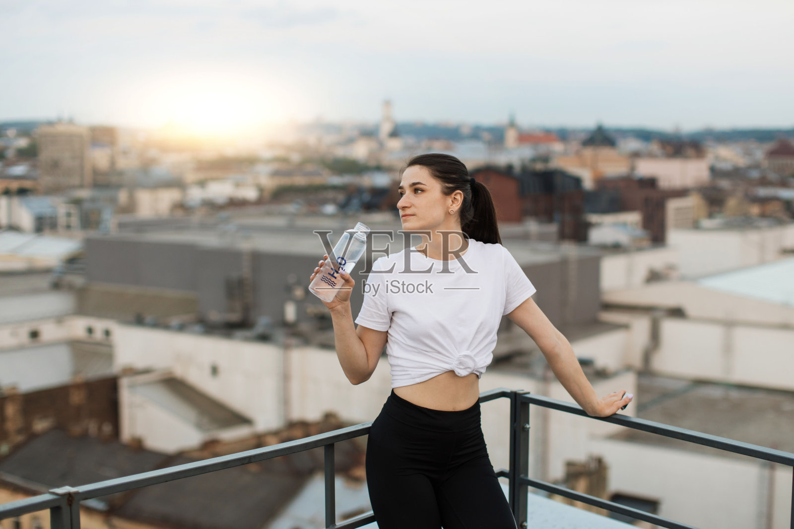 瑜伽行者拿着水瓶在楼顶看日落照片摄影图片