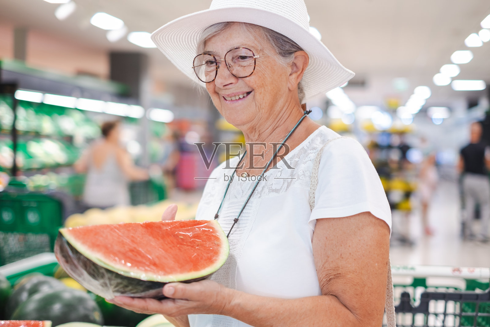 带着帽子微笑的老顾客女士在超市挑选新鲜水果，挑选了半个西瓜。领取养老金的老人注意到物价的上涨照片摄影图片