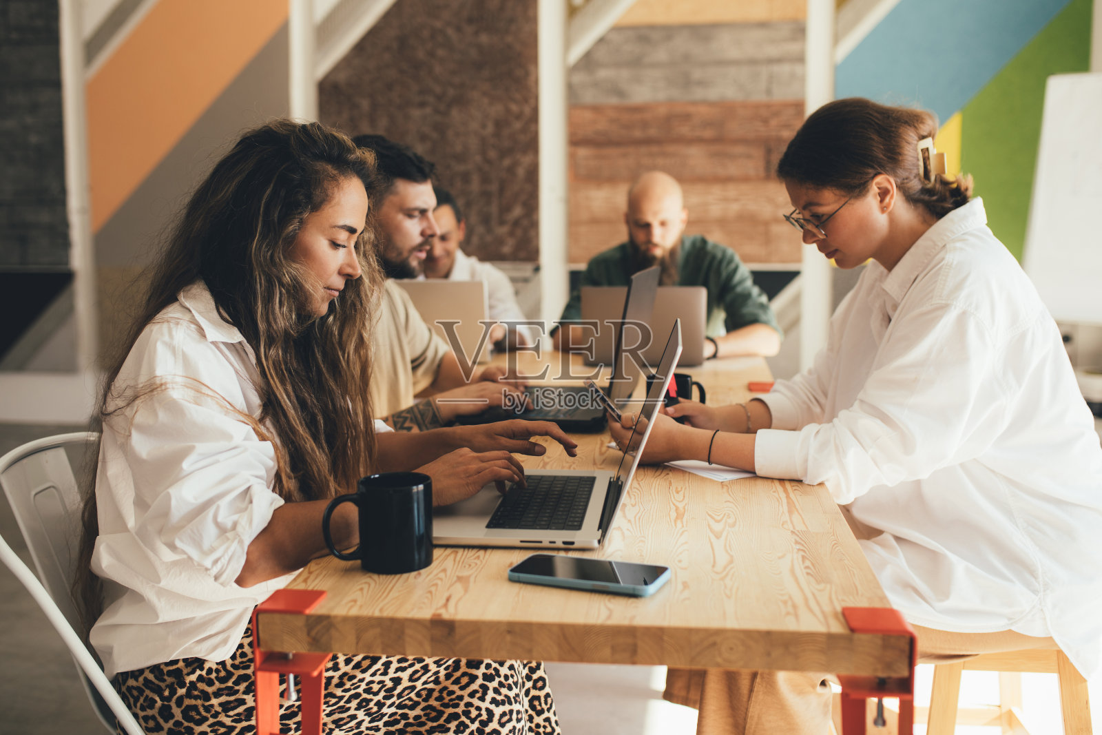 同事们坐在现代化的办公室里，用笔记本电脑工作。照片摄影图片