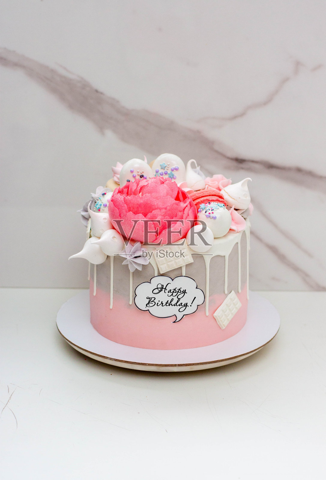 美丽优雅的灰色和粉红色蛋糕，装饰有融化的白巧克力，杏仁饼，可食用的牡丹花和蛋白霜之吻照片摄影图片