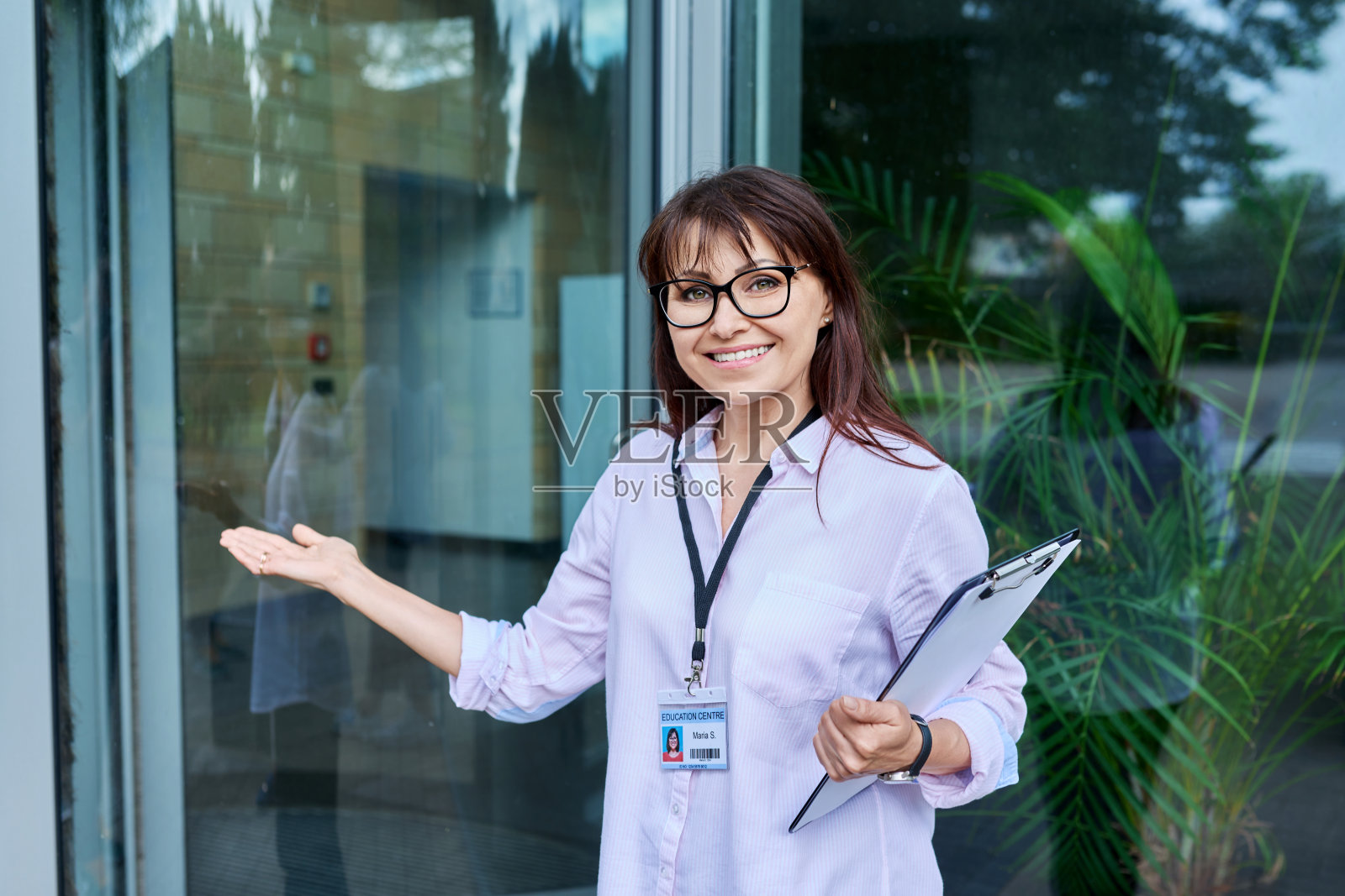 大楼玻璃门附近，带着写字板微笑的女教师肖像照片摄影图片