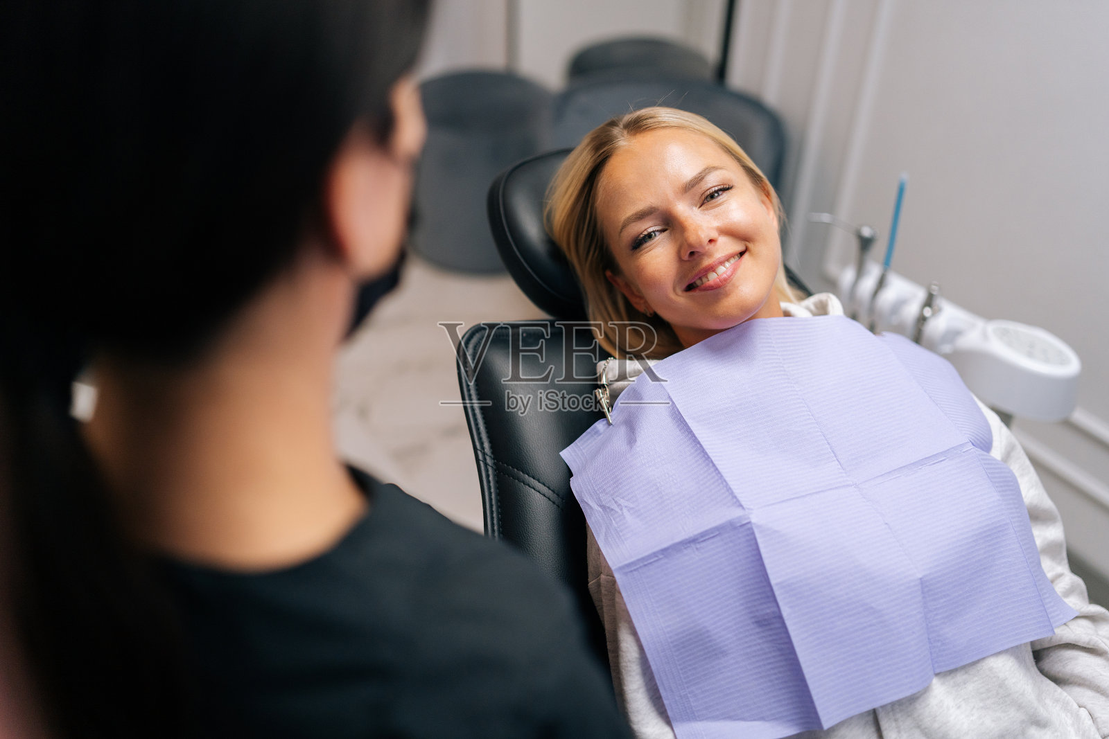 有牙齿问题的快乐年轻女病人，在检查和咨询时与不认识的牙科医生谈话的特写正面照片摄影图片