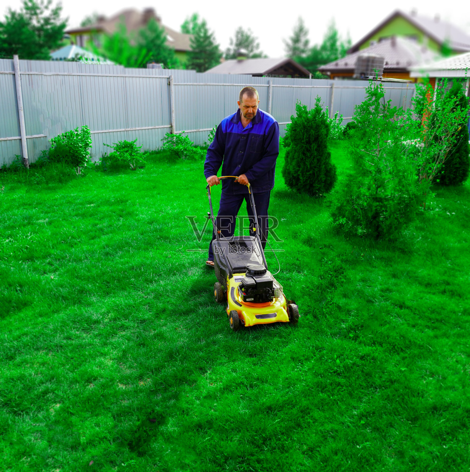 这个人正在花园里干活。用割草机割草。照片摄影图片