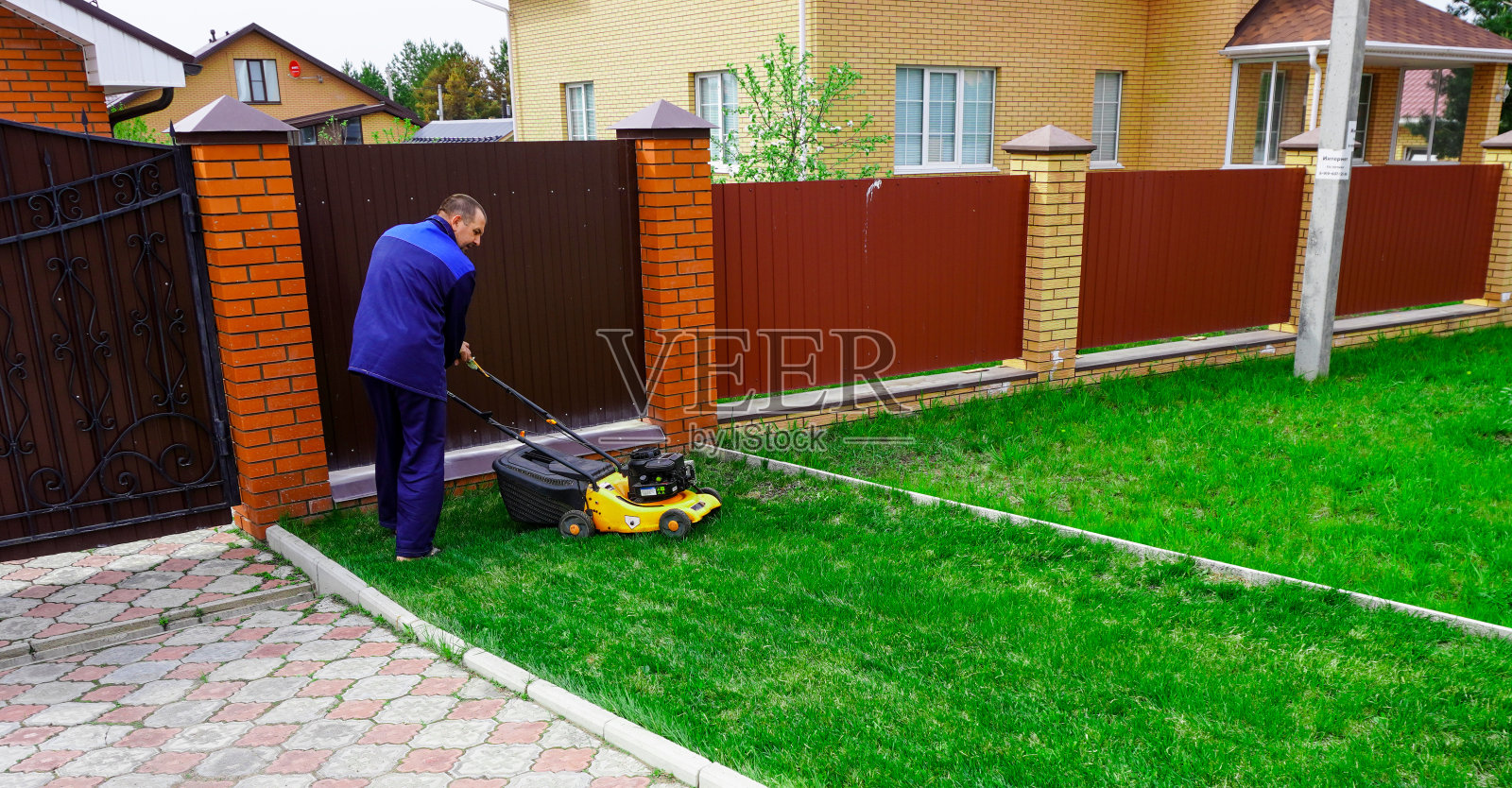 这个人正在花园里干活。用割草机割草。照片摄影图片