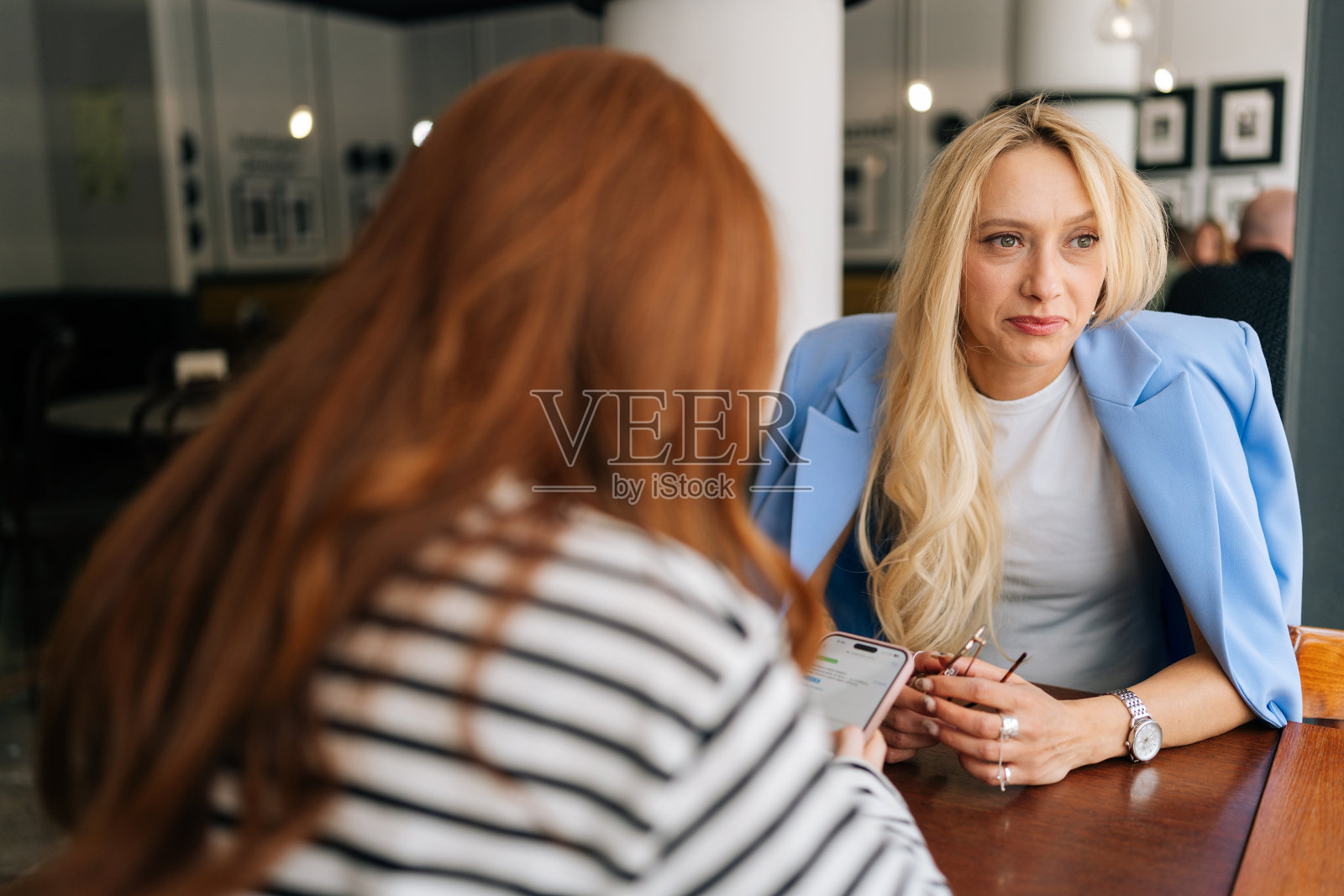 一个无法辨认的红发女人和一个金发的女性朋友聊天的后视图，他们在一家舒适的餐厅喝咖啡照片摄影图片
