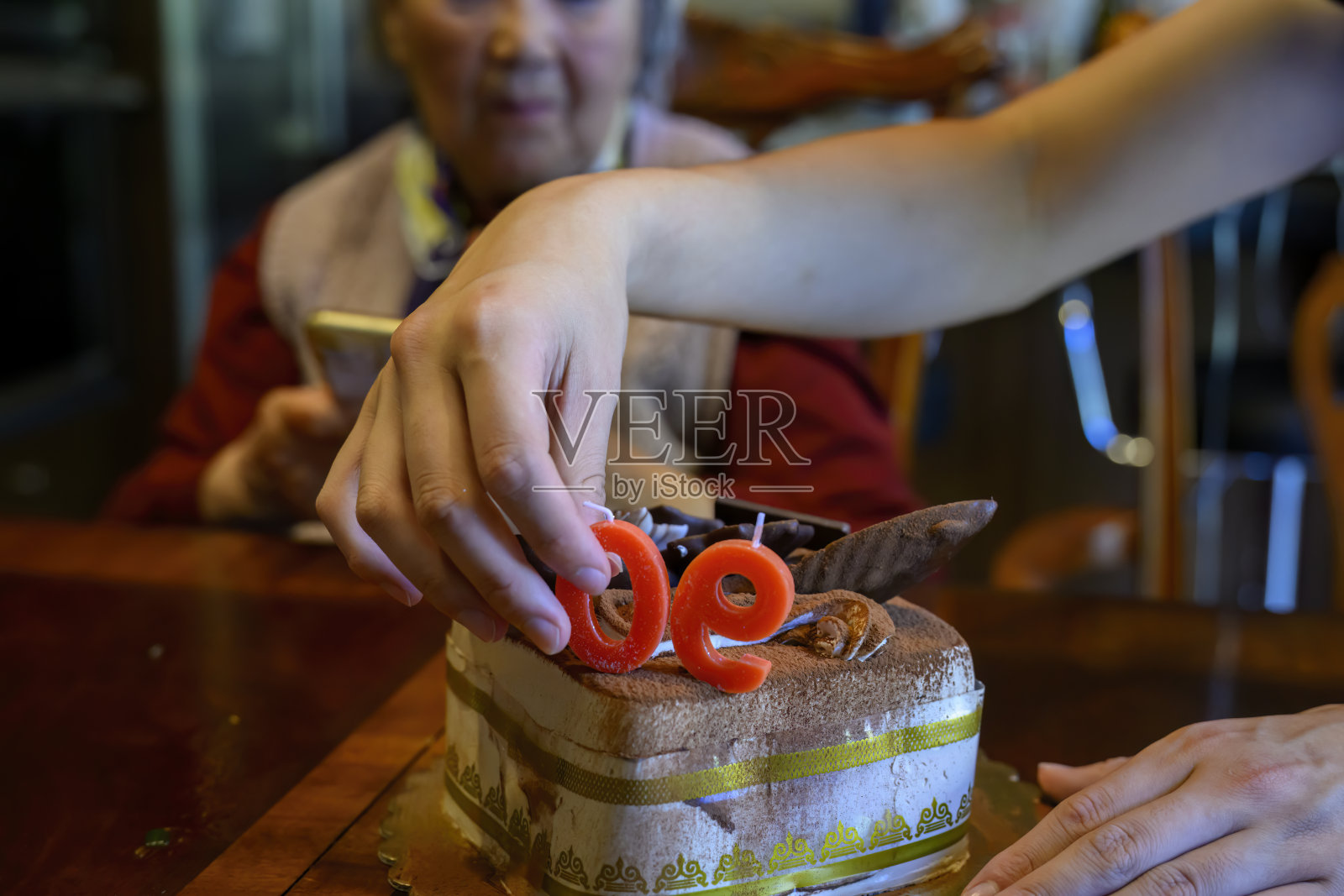 一个年轻人的手把蜡烛放在蛋糕上，庆祝祖母的90岁生日。照片摄影图片