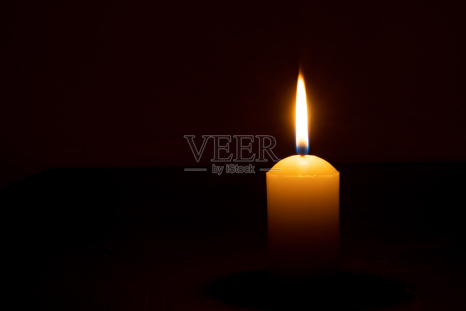 在圣诞节、葬礼或纪念仪式上，在教堂的桌子上，黑色或深色背景上，单支燃烧的蜡烛火焰或光在大黄色蜡烛上发光。照片摄影图片