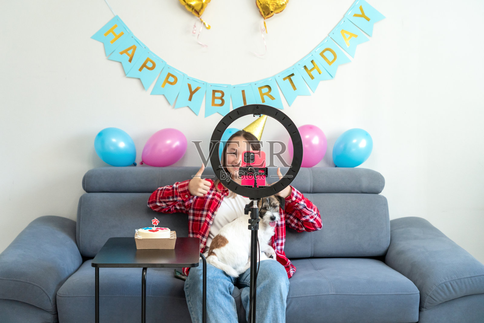 一个十几岁的女孩带着她有趣的宠物狗庆祝她的生日，并在家里拍了一段视频。Z世代达人玩视频自拍拍秀app分享病毒故事。照片摄影图片
