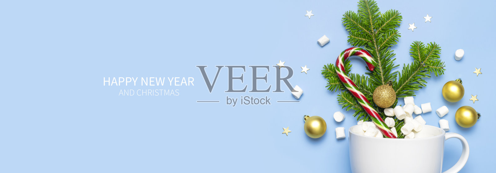 圣诞拐杖糖，绿色冷杉枝，金色的球，五彩星星，棉花糖白色的陶瓷杯在蓝色的背景上平铺顶视图。创意新年理念。节日装饰，节日贺卡2021照片摄影图片