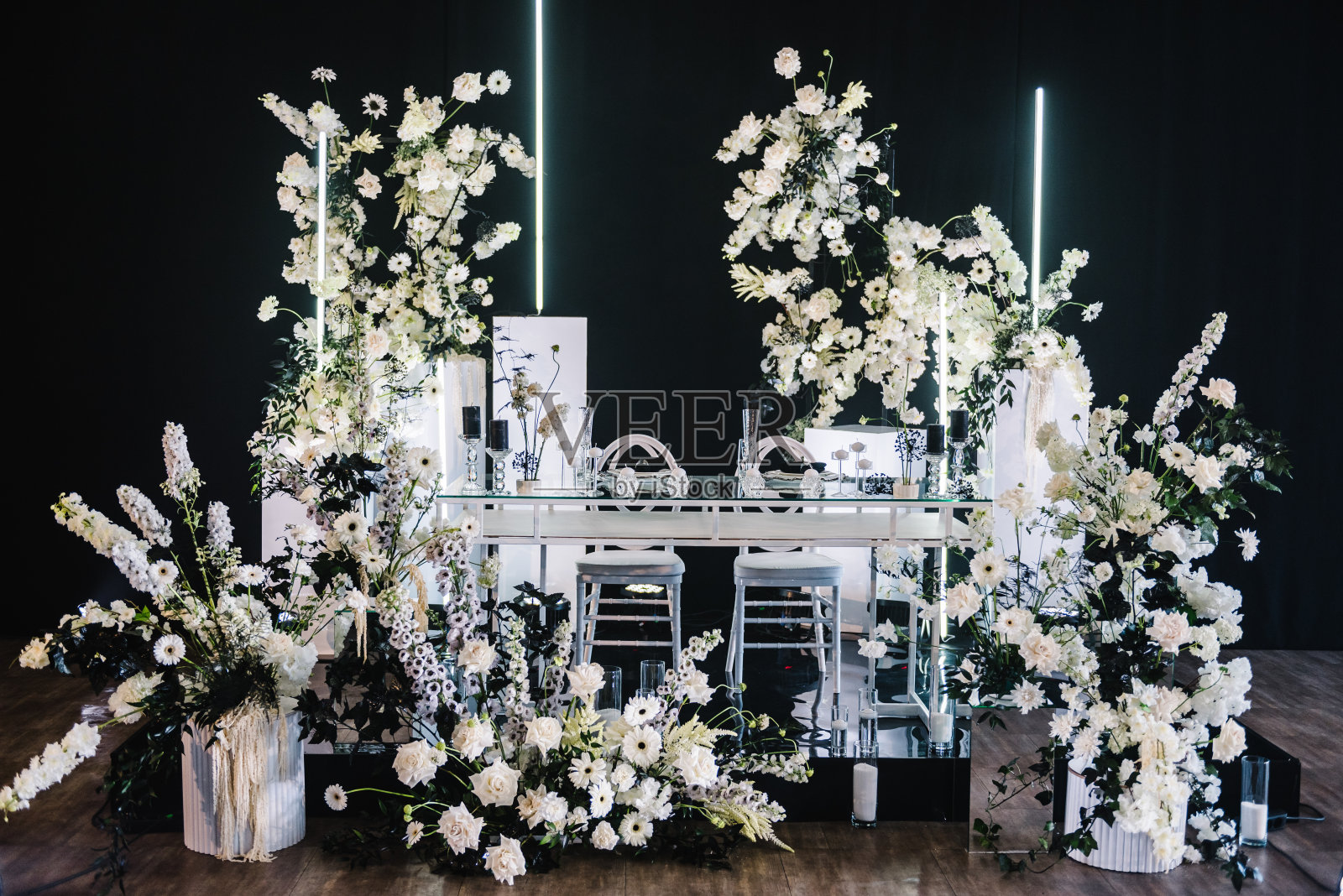 新婚夫妇在婚宴宴会厅的餐桌。节日的餐桌用拱形装饰组成鲜花和绿色植物，黑色的蜡烛在大厅餐厅。奢华的银色装饰。摆桌子，接待。照片摄影图片