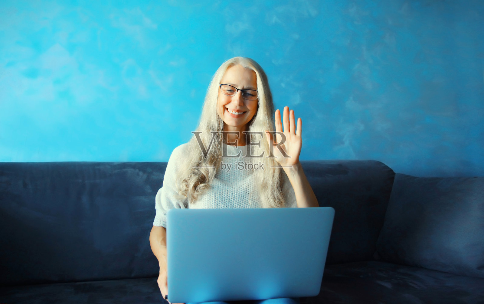 快乐的中年妇女用笔记本电脑工作，欢迎坐在家里房间的沙发上通过视频通话进行交流照片摄影图片
