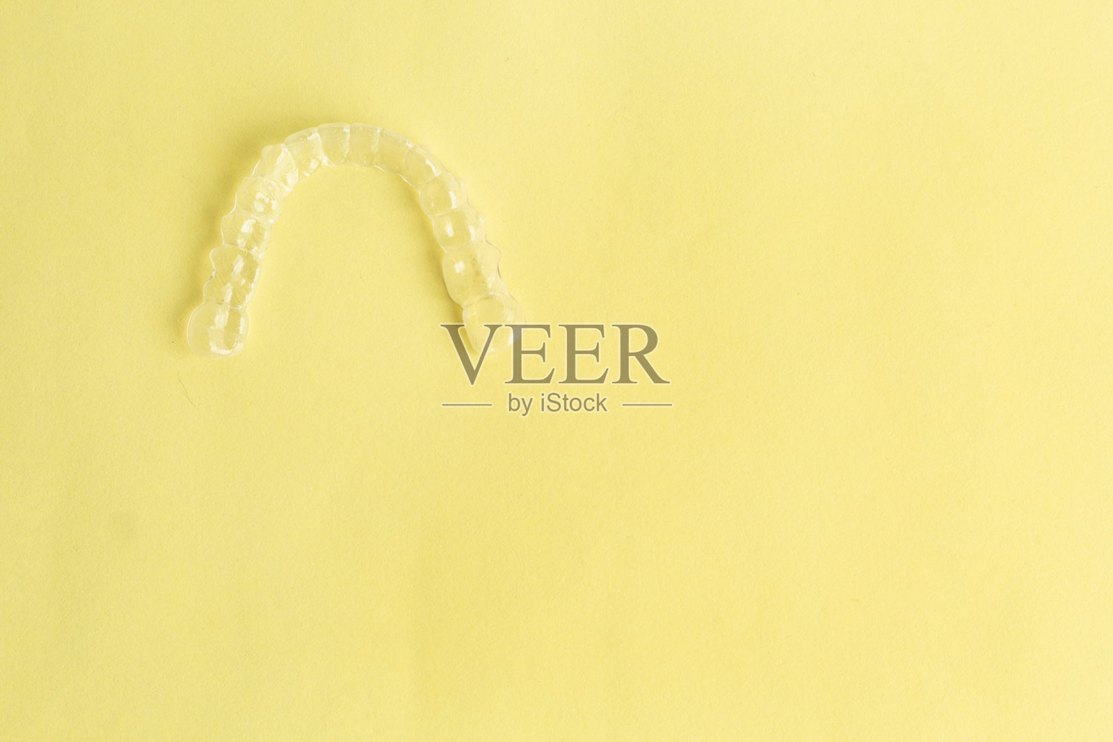 黄色背景的隐形牙齿矫正器或透明牙齿矫正器。牙科医生在诊所进行的牙齿矫正美容治疗……照片摄影图片