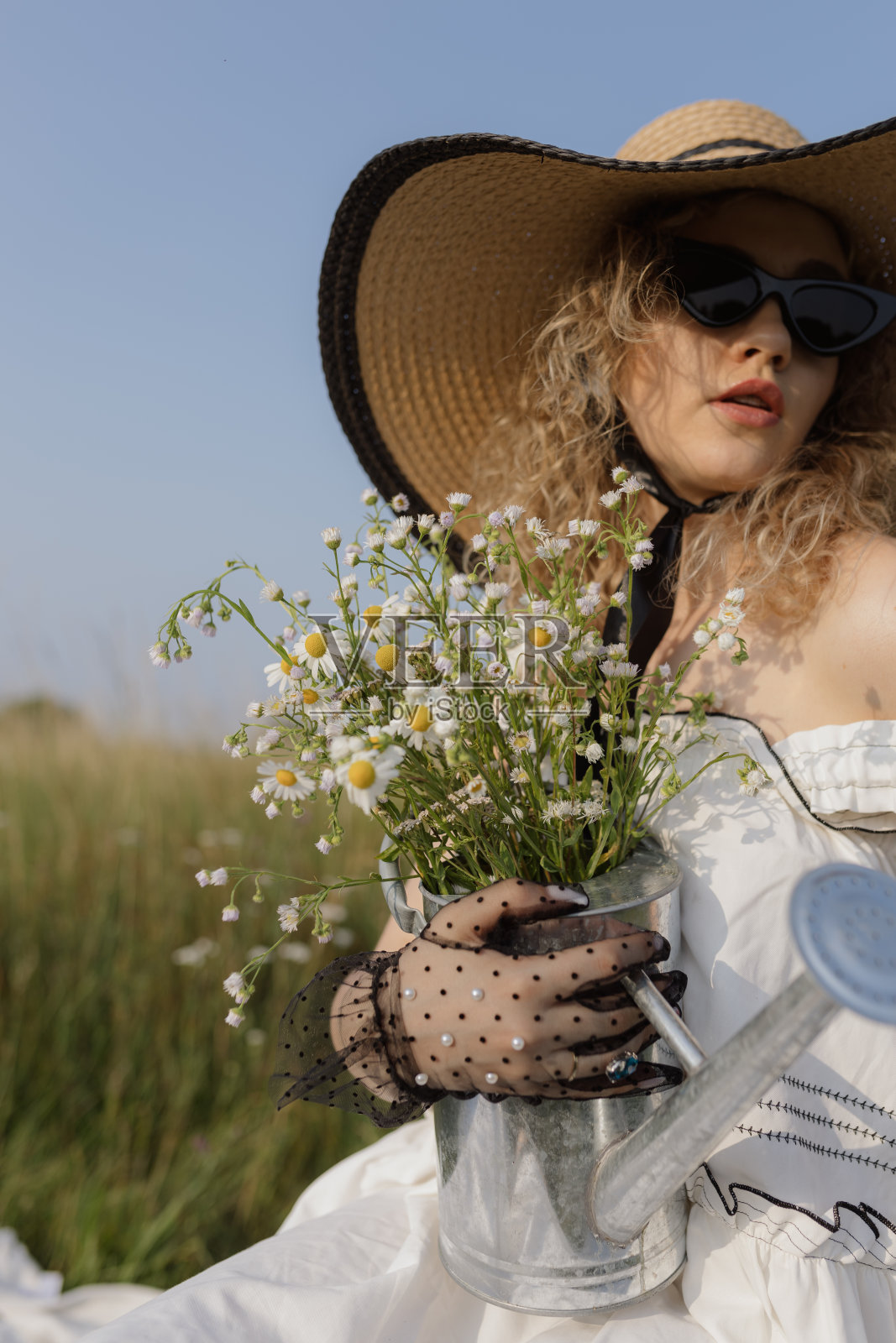 戴着帽子的时髦女人的肖像，她的手戴着黑色蕾丝手套，手里拿着一束雏菊。照片摄影图片