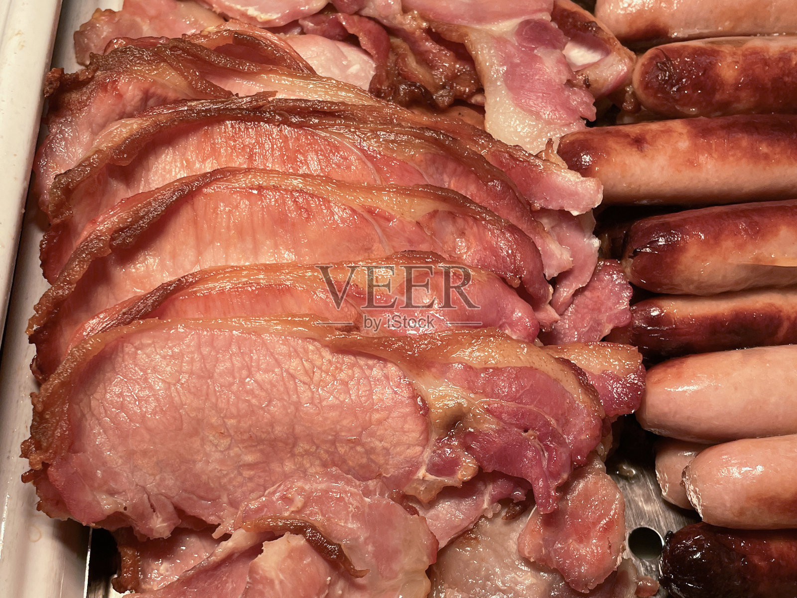 全英式自助油炸早餐食材，在加热灯下，上桌的一排排培根片和香肠，高架视图照片摄影图片