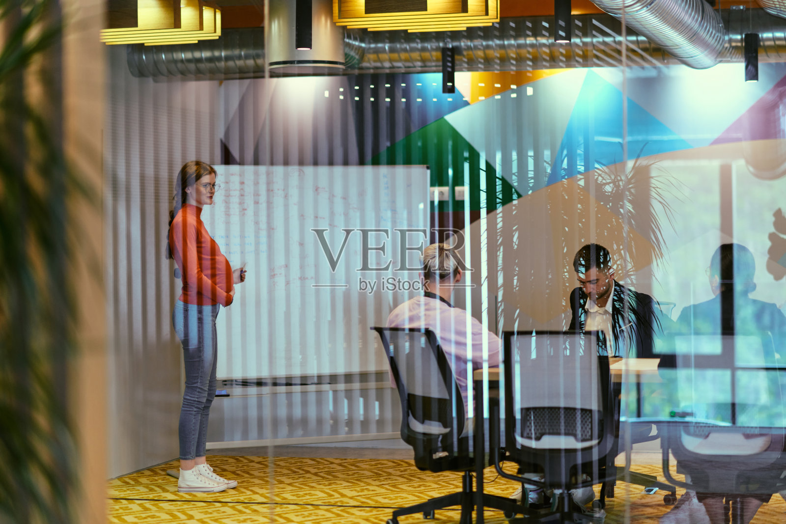 一位自信的橙发怀孕女商人在现代玻璃办公室里向同事展示她的商业计划，体现了创业和创新照片摄影图片