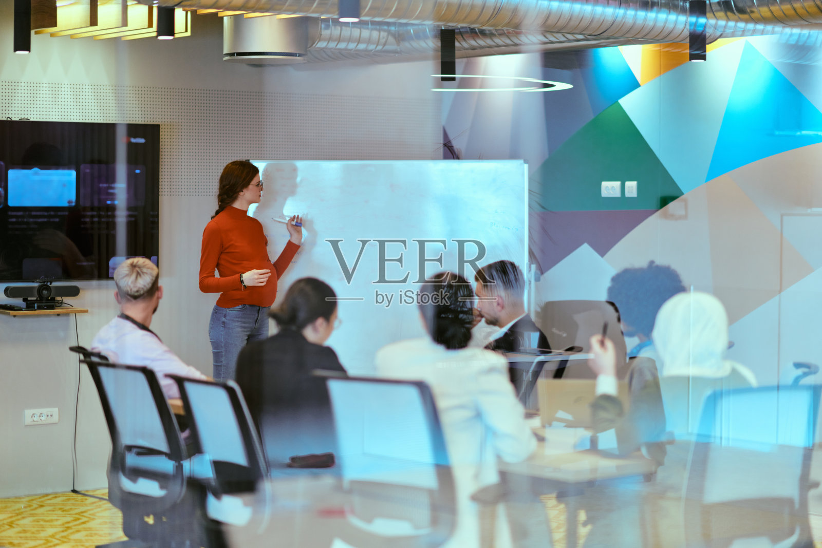 一位自信的橙发怀孕女商人在现代玻璃办公室里向同事展示她的商业计划，体现了创业和创新照片摄影图片