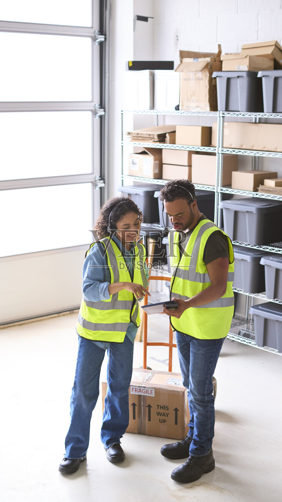 在仓库中使用数字平板电脑和唐氏综合征男同事的女人，他们都戴着耳机照片摄影图片