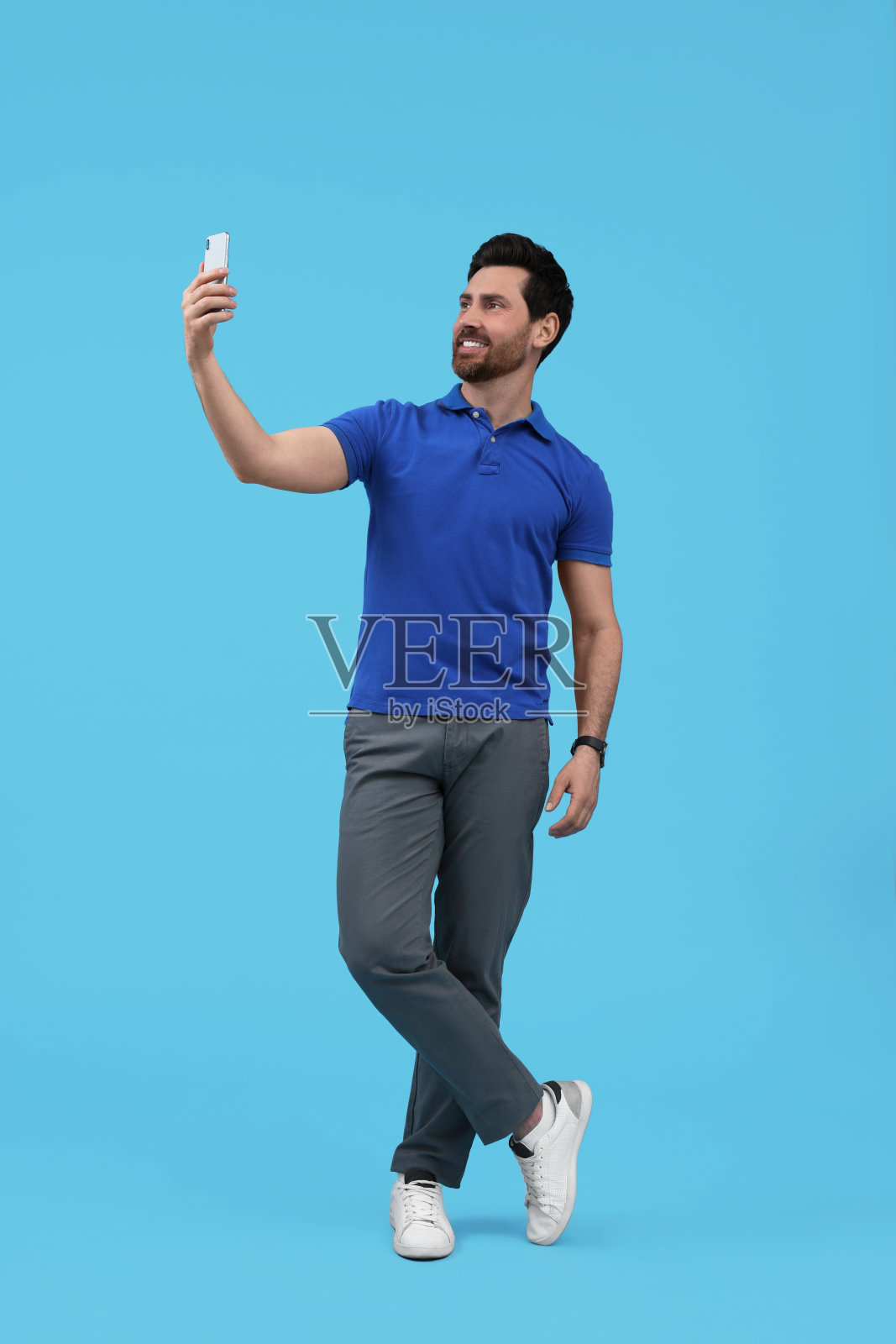 微笑的男子在浅蓝色背景下用智能手机自拍照片摄影图片