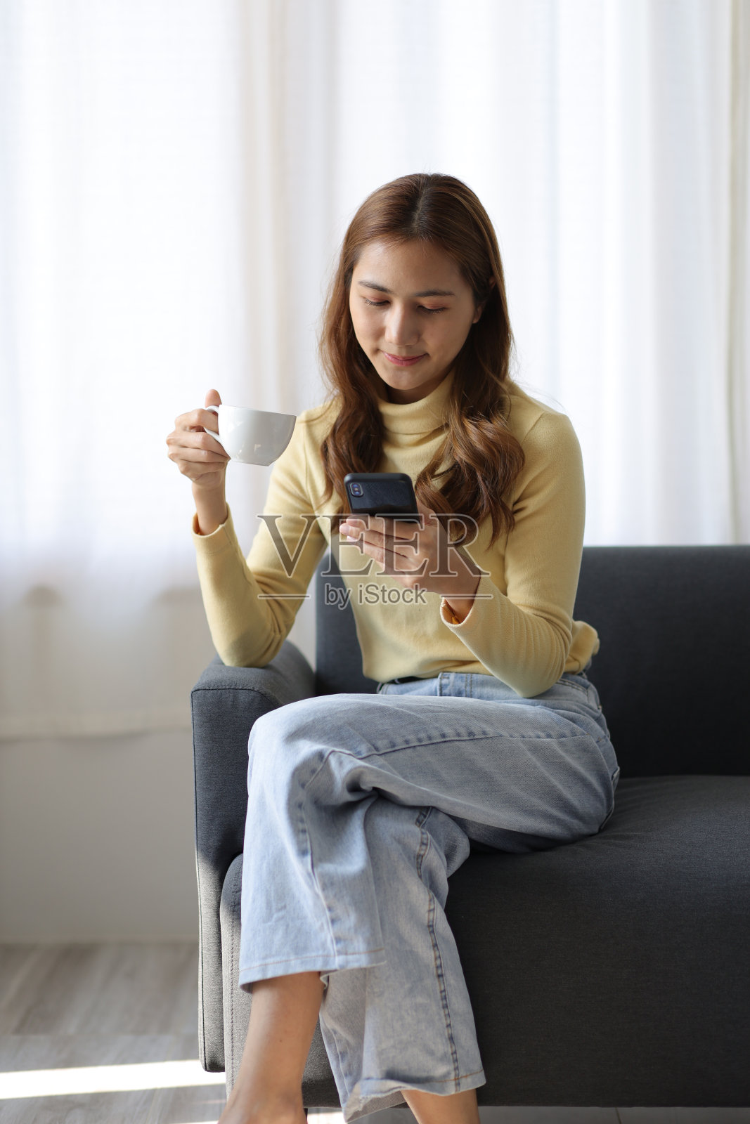 快乐的女人一边在家喝咖啡，一边用智能手机收发朋友的短信。照片摄影图片