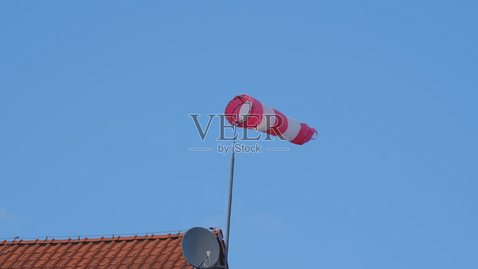 安装在通航机场大楼楼顶的红白条纹风袜风锥风套指示器，向驾驶飞机的飞行员显示风速和风向照片摄影图片