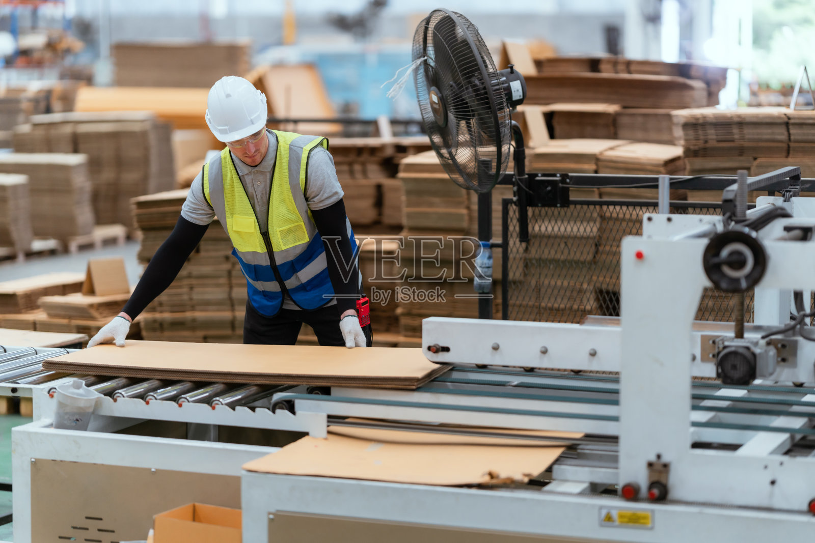 一名男性员工正在仓库里使用机器缝制纸板箱。整理纸板箱照片摄影图片