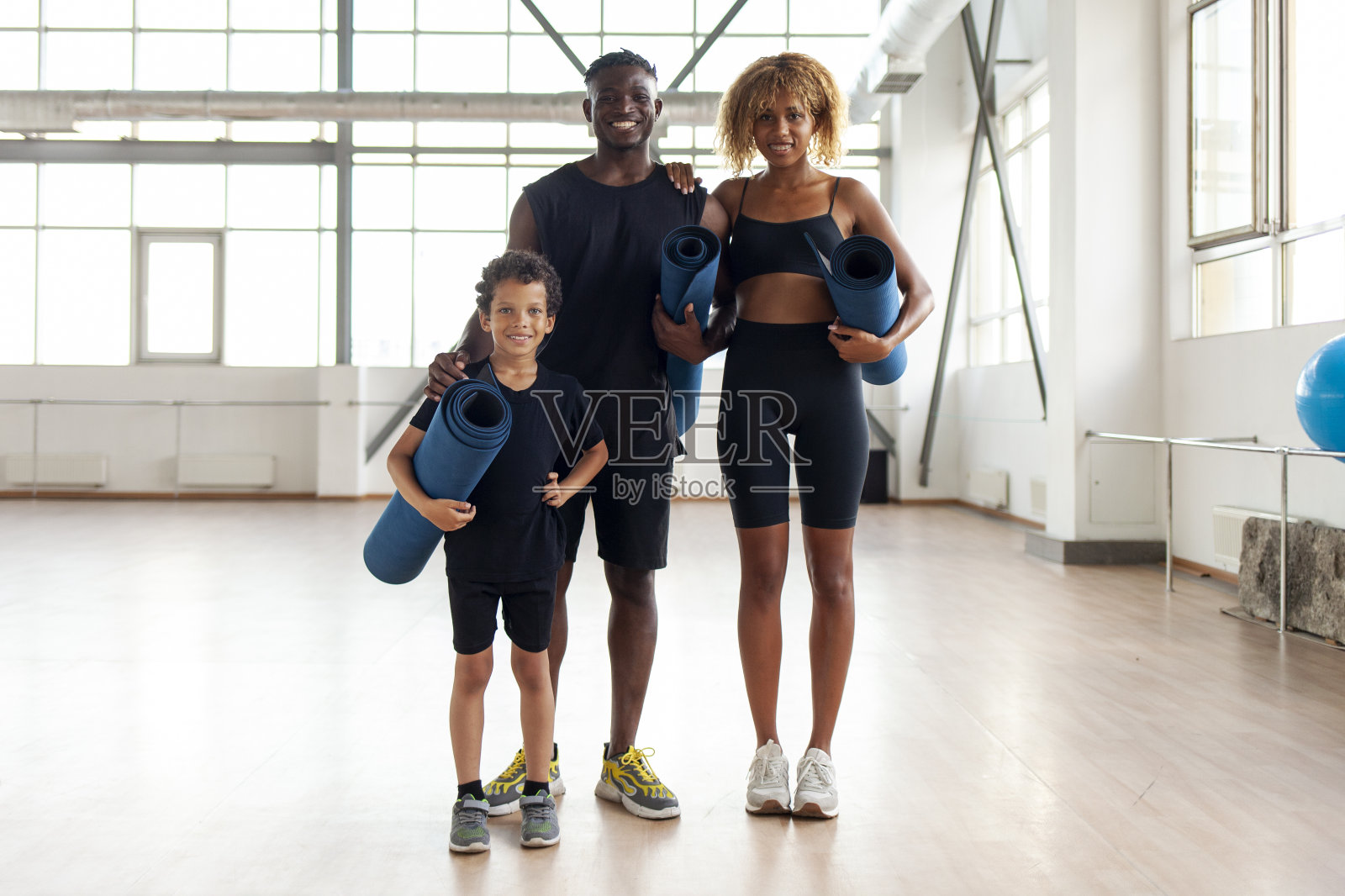 非裔美国家庭穿着运动服，拿着瑜伽垫站在健身房，爸爸妈妈和儿子在健身锻炼照片摄影图片