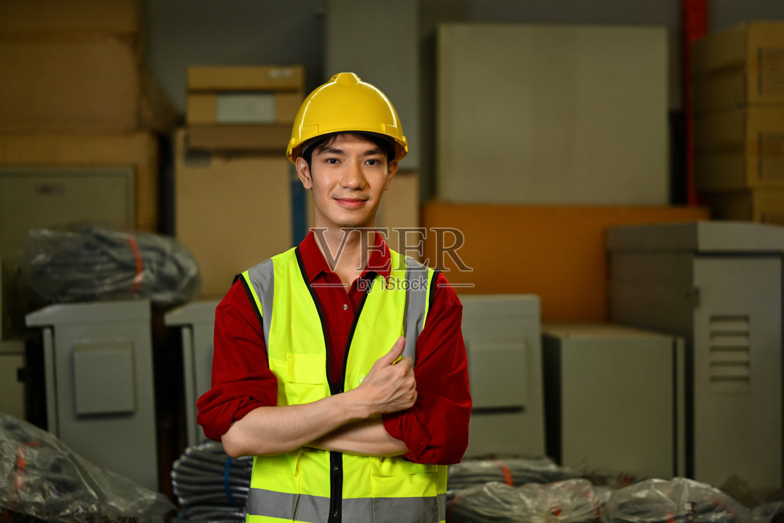 自信的亚洲男性仓库工人，戴着安全帽和背心，对着镜头竖起大拇指，微笑着照片摄影图片