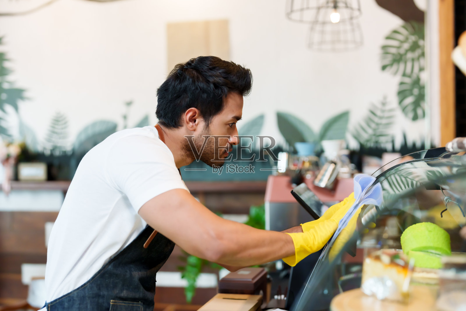 一个英俊的西班牙男人经营着家里的小咖啡店，帮一个漂亮的亚洲园丁打扫玻璃柜。准备早上开一家咖啡店，准备迎接顾客照片摄影图片
