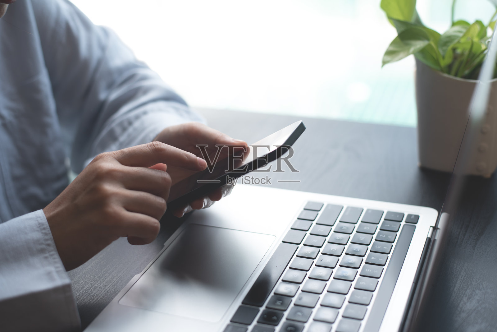 商务女性坐在办公桌旁用手机上网，在家用笔记本电脑办公，商务休闲装，远程办公，在家办公，近距离照片摄影图片
