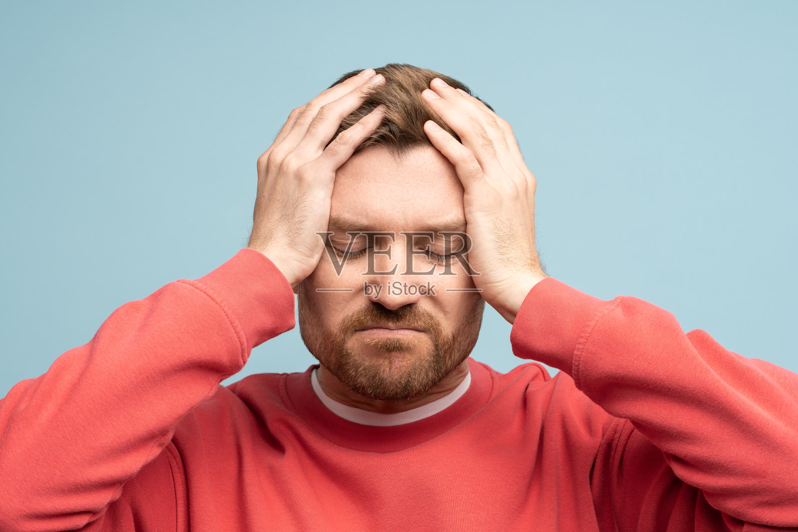 烦躁的悲伤男子头部不适，在蓝色墙壁背景的工作室里感到头痛照片摄影图片